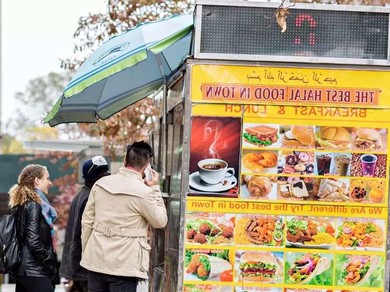 清真食品卡车上有五颜六色的食品海报，人们在排队